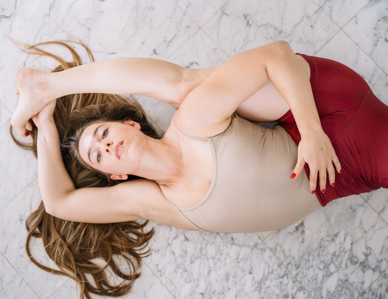 Woman performing a flexible yoga pose indoors on a tiled floor, showcasing balance and strength.